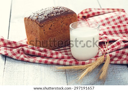 Freshly baked bread with spikelets of wheat and glass of milk on a red and white cloth on a wooden boards. close up