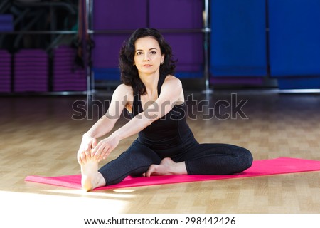 Nice girl with dark curly hair wearing on black shirt and leggings doing exercises on pink yoga mat on a sports equipment background at the gym