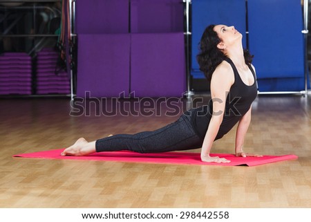 Fitness woman with curly short hair wearing on black shirt and leggings make yoga stretching exercise on pink yoga mat on a sports equipment background at the gym