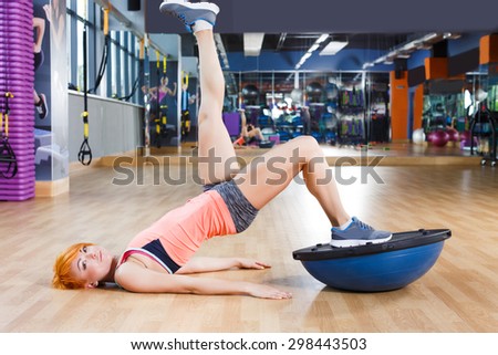 Redhead pretty fitness girl is doing exercises with bosu ball near the mirror in the gym near the mirror