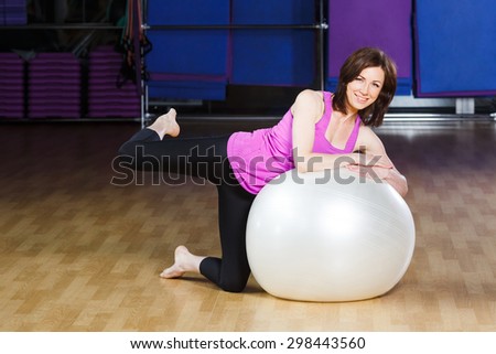 Young, beautiful, fitness woman with short hair wearing on violet shirt does exercises on a white fitball at the gym