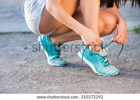 Running and sport concept. Female athlete, wearing in gray shorts, tying blue sport footwear laces on road before training, close up