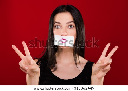 Lovely young girl, wearing on black shirt, posing with piece of paper with the imprint of her lips, on the red background, in studio, waist up
