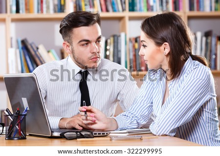 Business woman and man, wearing in classic shirts, discussing in modern office. Woman wearing in white and blue striped blouse and man is wearing in white shirt and black tie, waist up