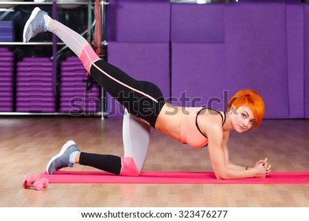 Young fitness woman, with short haircut, wearing in top, sneakers and leggings, does exercises on pink yoga mat, in the gym, full body