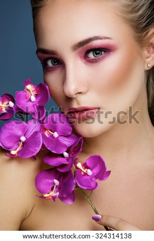 Portrait of a beautiful blonde woman with delicate makeup holding orchid in her hand, close up. Fashion photo