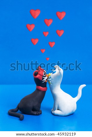 Two sweet plasticine black and white cats in love with each other. Blue copyspace for greeting text