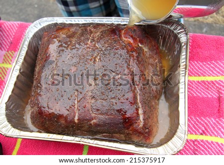 pouring juice and sauce over a smoked cooked pork roast in a pan