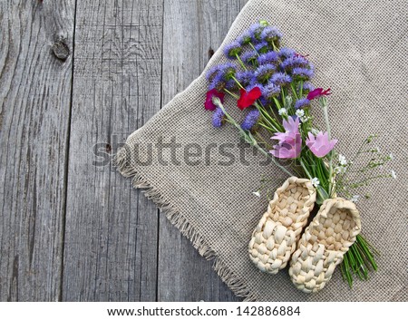Rural still life with decorative sandals made of bark and with a bouquet of wild flowers on a wooden table