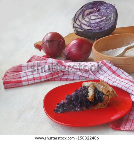 Portion of vegan pie on the background of the ingredients: red cabbage and onions