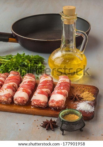 Cooking of lunch on meat rolls on a cutting board on a background of the frying pan, sunflower oil and onions with spices