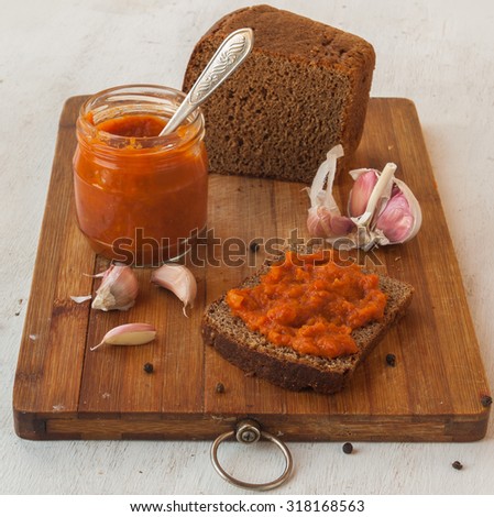 Rye bread spread with spicy stuffed peppers, tomatoes, carrots, garlic and apples on a cutting board