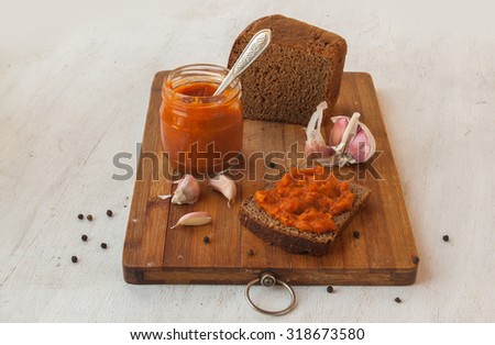Rye bread spread with spicy stuffed peppers, tomatoes, carrots, garlic and apples on a cutting board