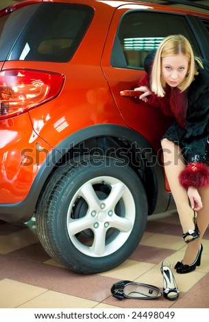 attractive young white girl changing shoes near new red off-road cars in office looking in shot