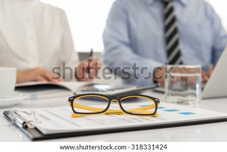 Marketer\'s desk with analysis Report , glasses and people in office.