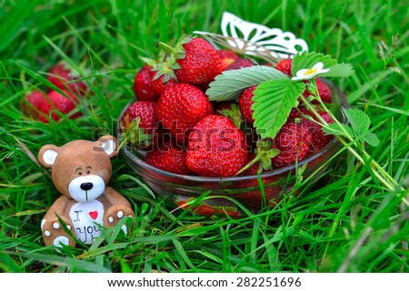 Composite photo - wallpaper with the image of bowl with fresh and tasty red strawberry, souvenir clay toy bear with heart and the words \