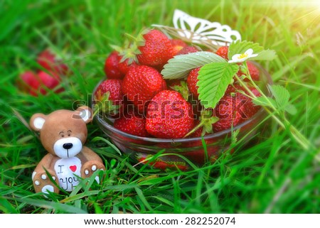 Composite photo-wallpaper with the image of bowl with fresh and tasty red strawberry, souvenir clay toy bear with a heart and the words \