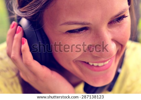 Beautiful girl in a park listening to the sound of music in the headphones (soft focus)