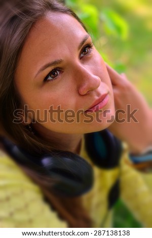 Beautiful girl in a park listening to the sound of music in the headphones (soft focus)