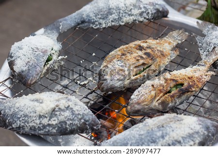 Salt Crusted Grilled Nile Tilapia Fish on Grate on charcoal stove Clear focus on specific areas of the image./ soft Focus