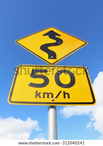 Black and yellow '50 km/h' and 'windy road' signs against a blue sky