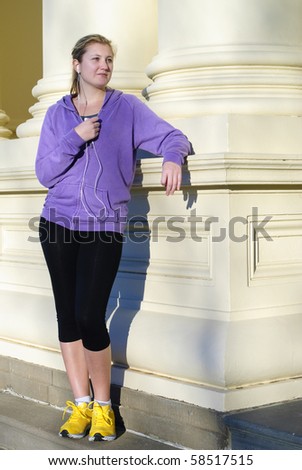 Jogger wearing purple top and yellow sneakers listening  to music and leaning on city steps after run