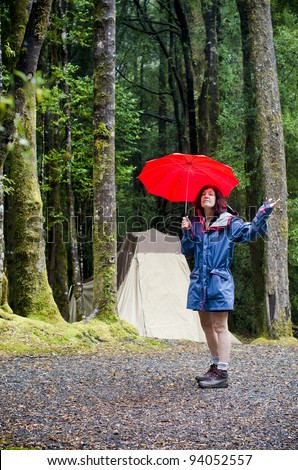 Female camper holding red umbrella checking for rain near rain forest trees near Queenstown, Tasmania, Australia