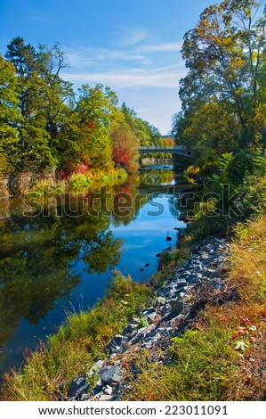 River bank in early autumn. A Bridge in the back. Water reflecting colorful trees.