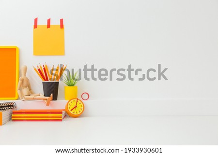 Creative desk in kids room with yellow frame mock up, plant and notebooks, note on the wall and many yellow and orange supplies.