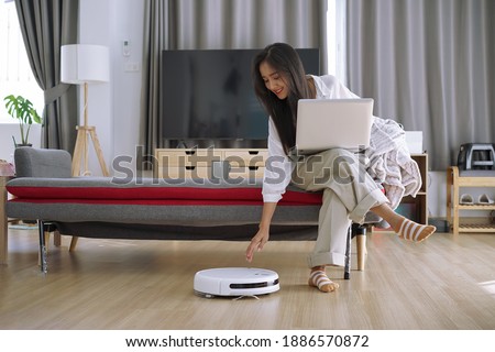 Robotic vacuum cleaner cleaning the room while woman working with laptop computer on sofa at home.