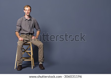 young man sitting on a stool on a blue background