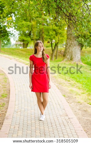 The young beautiful girl with freckles and red dress standing on the track in the park green background