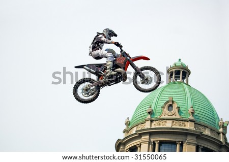Motocross rider performing extreme jump next to cupola of old stylish building