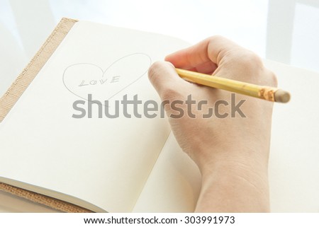 Pencil in hand writing something on white paper book background warm color tone style