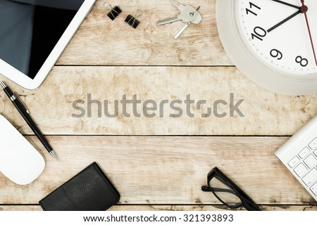 office desk from top view ,black bag,mouse,keyboard,tablet ,pen ,black plastic glasses,clip,clock with wood  background.