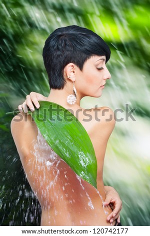 Beautiful naked back of young woman closing by palm leaf off splash of water against wet green background