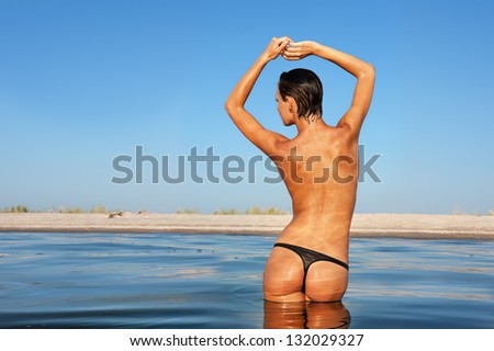Beautiful figure of young tan woman standing in sea water