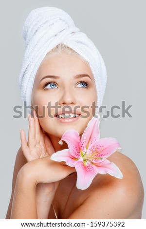 Close-up face of young beautiful woman in white towel with pink lily on gray background