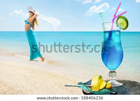 Blue Curacao cocktail on background of sea beach with pretty girl in blue long skirt. Summer concept