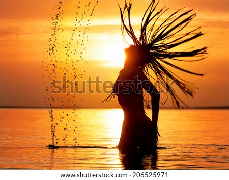 Beautiful female silhouette with splash of sea water against  sunset background
