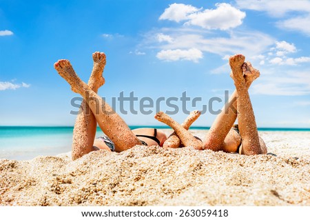 Close-up legs of several girls lying on sandy beach and tanning in the bright summer sun