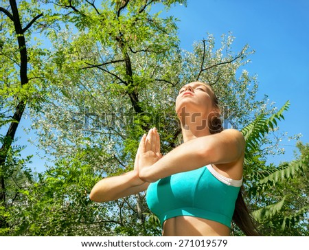 Young woman doing relaxation exercises against background of blue sky and green trees