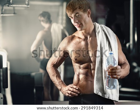 Portrait of young smiling muscular man with towel and bottle of water in gym after fitness workout