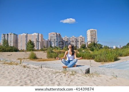 The young cute girl, in a pose of meditation against a city landscape