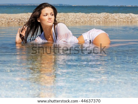 The beautiful young girl in wet clothes lies in water on seacoast