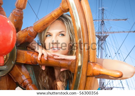 Portrait of beautiful young woman with steering wheel on sailing ship