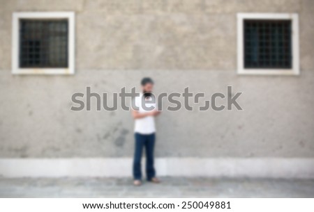 Man and his smart phone, wall on the background. Intentionally blurred editing post production background.