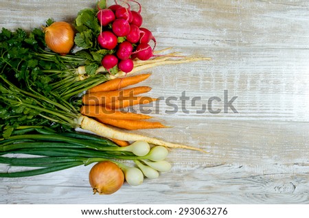Young spring vegetables on wooden background. Carrots, radish, parsley, onion - fresh harvest from the garden