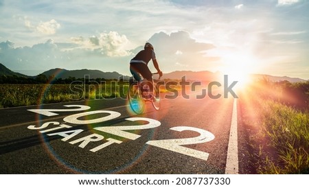 New year 2022 or start straight and beginning concept.Blurry Man ride on bike and word 2022 start written on the road at sunset add lens flare.Concept of challenge or career path,business strategy.