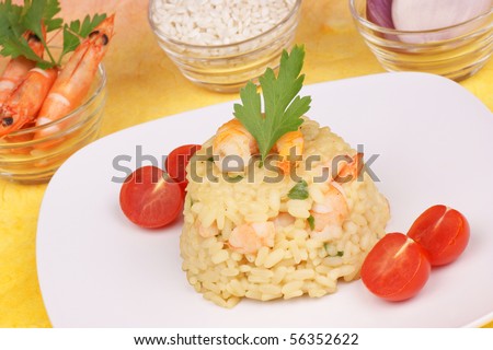 Risotto with shrimps served on a white plate. Rice, shrimps and shallots in small glass bowls are out of focus  in the background. Studio shot. Shallow DOF